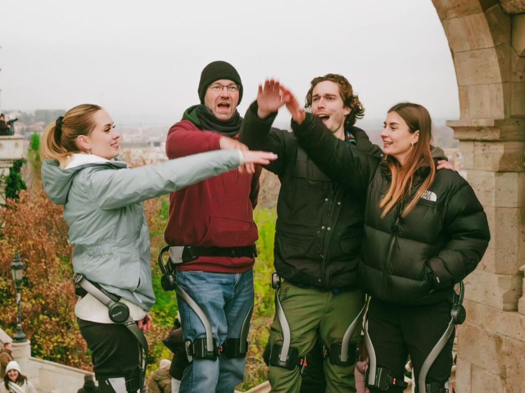 Four people wearing Hypershell exoskeletons high-fiving each other at the end of an exoskeleton tour in Budapest, Hungary.