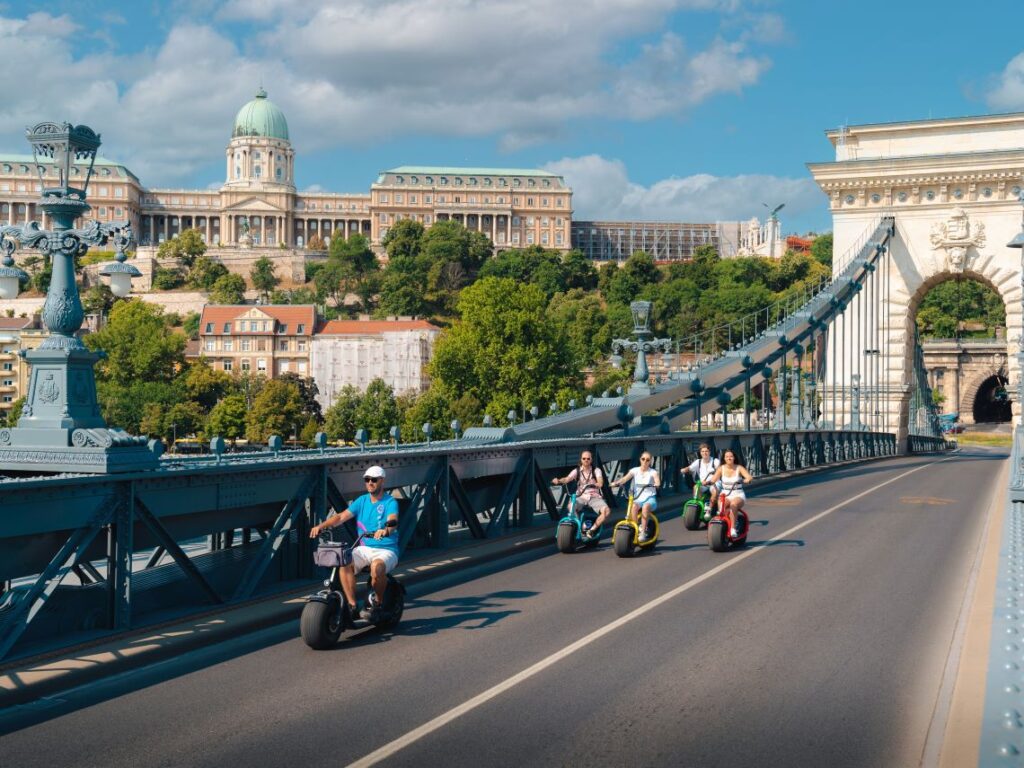 A group of guests and a tour guide crossing the Chain Bridge on e-scooters during an e-scooter tour in Budapest, Hungary