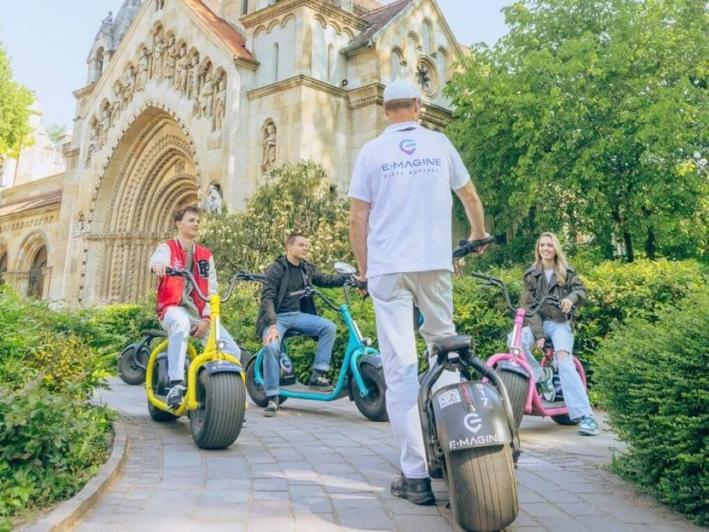 Four people on colorful e-scooters stopping inside Vajdahunyad castle during an e-scooter tour in Budapest, Hungary