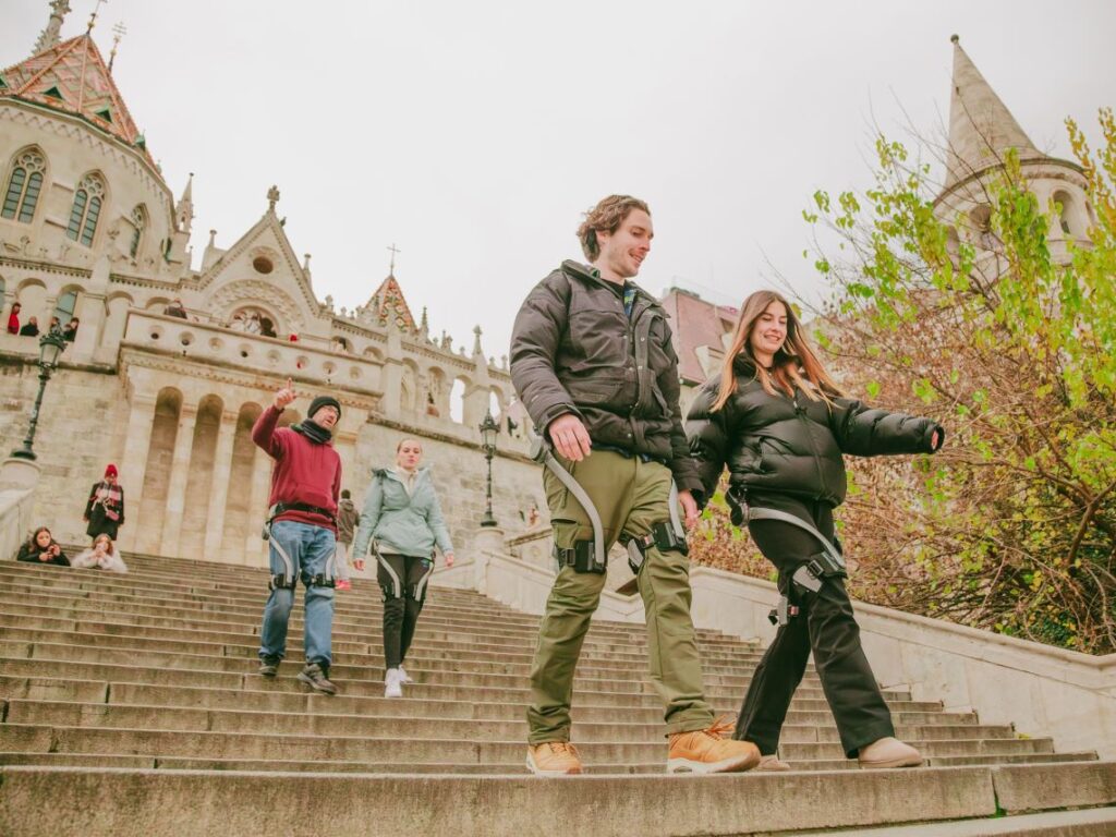 Four people wearing Hypershell exoskeletons walking down the steps in Buda Castle during a walking tour in Budapest, Hungary.