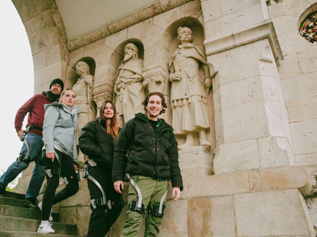Four people wearing Hypershell exoskeletons stopping for a picture during their exoskeleton walking tour in Budapest, Hungary
