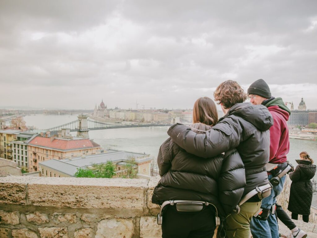 Three people wearing Hypershell exoskeletons admiring the panorama of the Chain Bridge during an exoskeleton tour in Budapest, Hungary