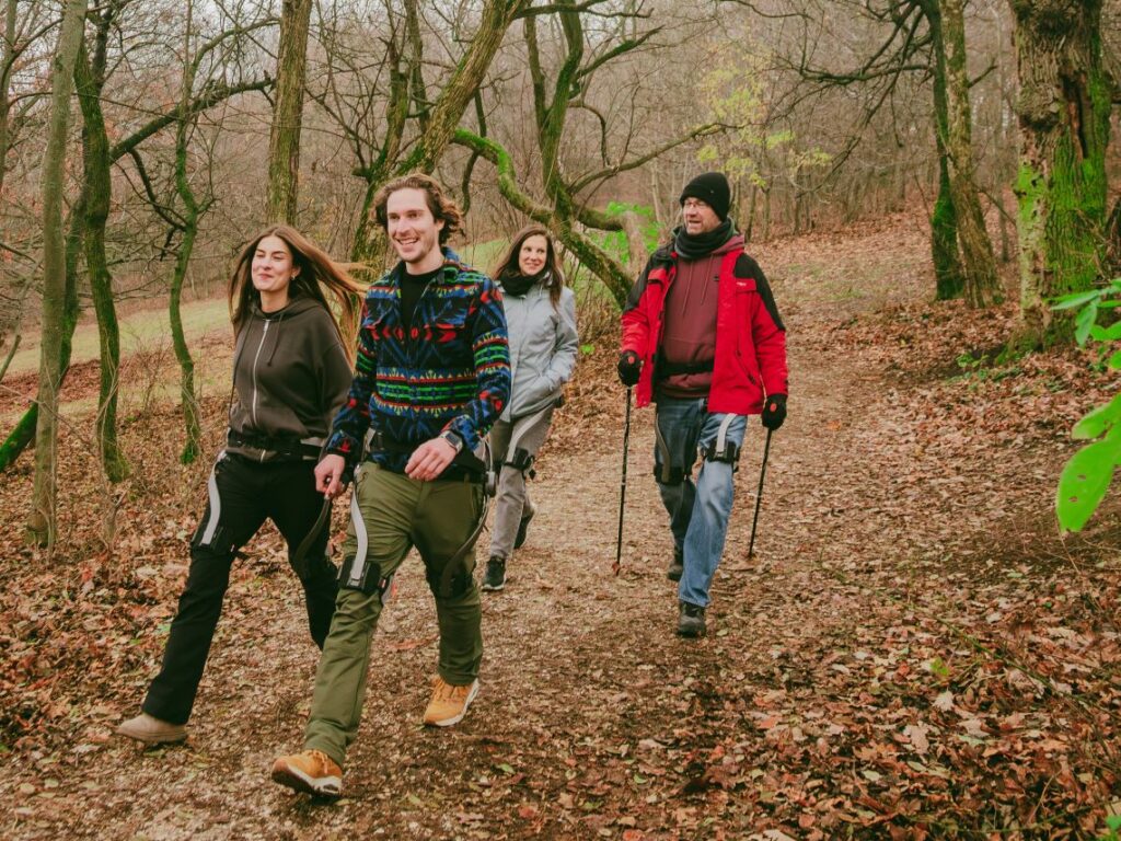 Four people walking happily wearing Hypershell exoskeletons in the woods near Budapest, Hungary